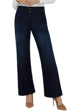 A model wearing dark blue wide-leg denim jeans with a button fly and front patch pockets, styled with a white ribbed top and tan high heels against a plain white background.