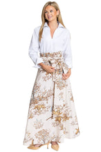 A woman modeling a white long-sleeve button-up shirt paired with a high-waisted, floor-length skirt featuring a brown and beige botanical floral pattern, set against a plain white studio background.